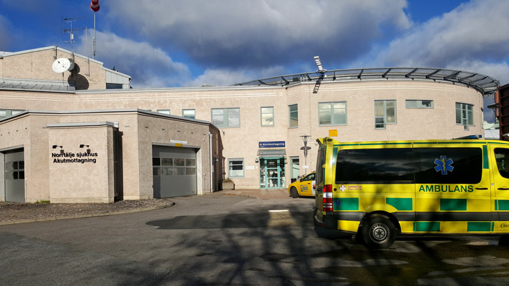 Ambulans framför tegelbyggnad. På en skylt på väggen står det Norrtälje sjukhus Akutmottagning. 