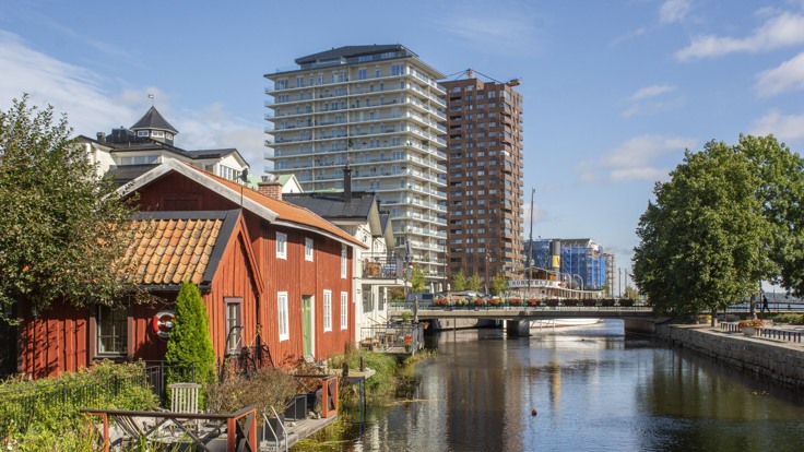 Rött trähus i förgrunden, vatten och två stora höghus