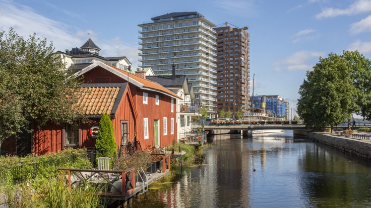 Rött trähus i förgrunden, vatten och två stora höghus