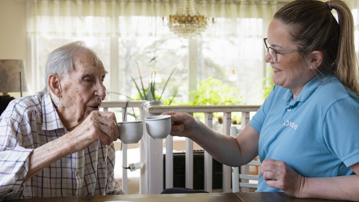 Äldre man och hemtjänstpersonal skålar med kaffekoppar