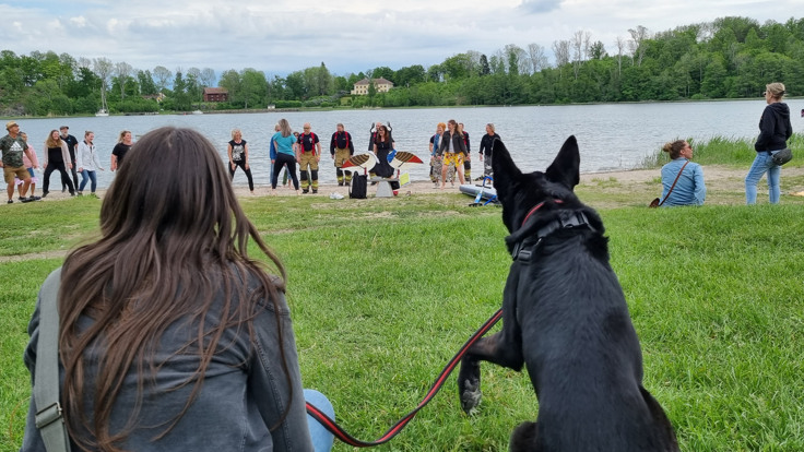 Kvinna och hund på gräsmatta vid vatten.