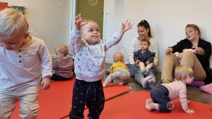 Kvinna blåser såpbubblor. Litet barn försöker fånga bubblorna. 