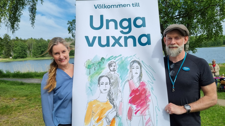 En kvinna och en man håller en banderoll med texten "Välkommen till Unga vuxna" mellan sig.