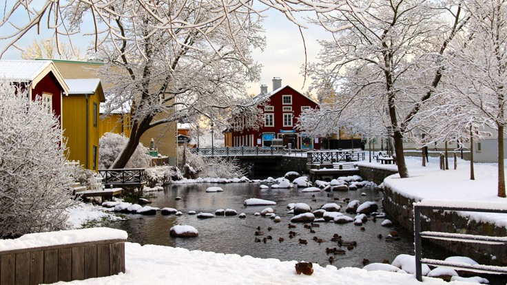 Trähus invid en å, snötäckt mark.